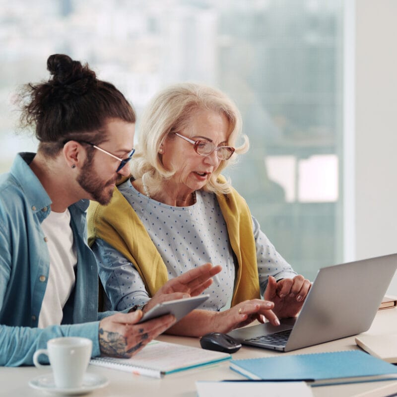 Member experience health plan navigation young man helping an older woman on a computer.