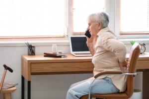 Senior woman with back pain talking by mobile phone at home